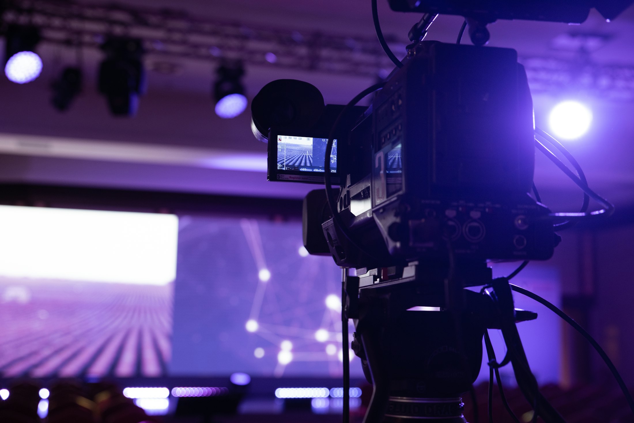 Broadcast camera on a tripod covering a live event stage
